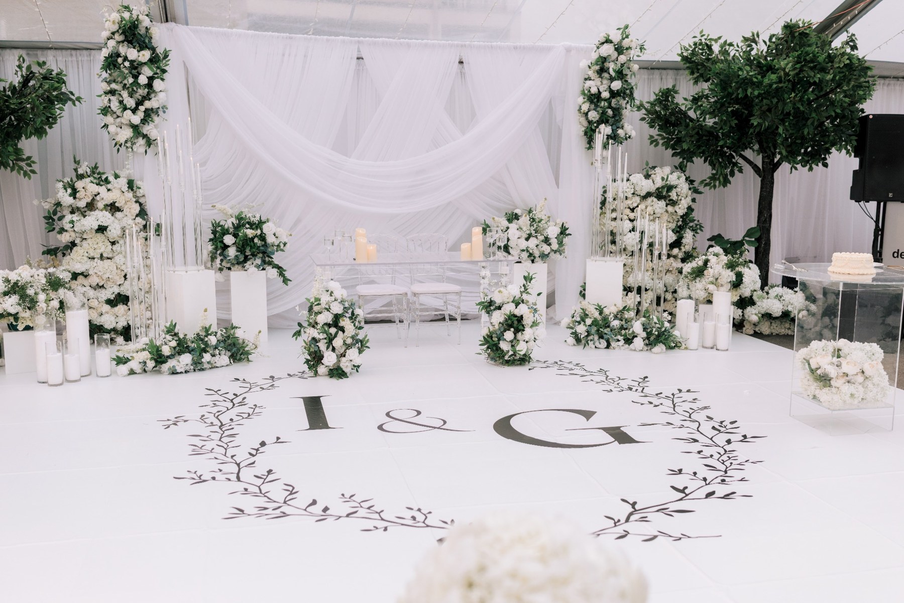 Past reception setup with a white dance floor, floral backdrop and head table beneath the tent